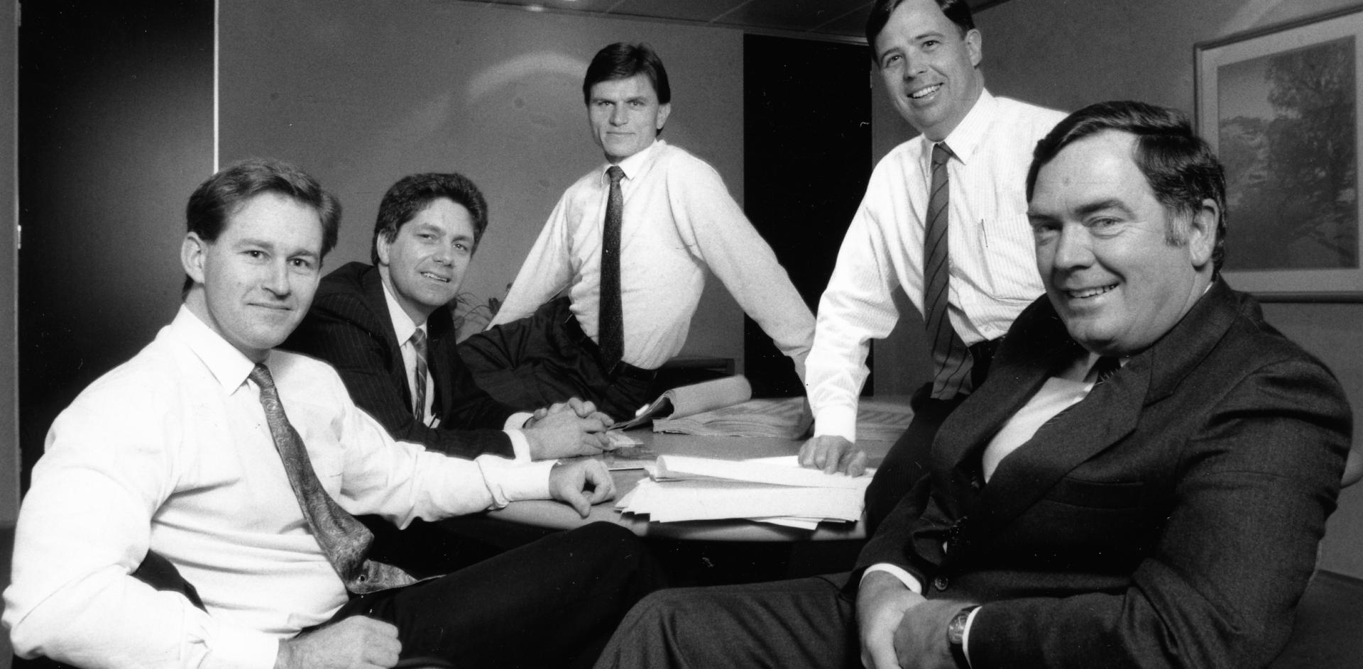 Black and white photograph of five men sitting around a table