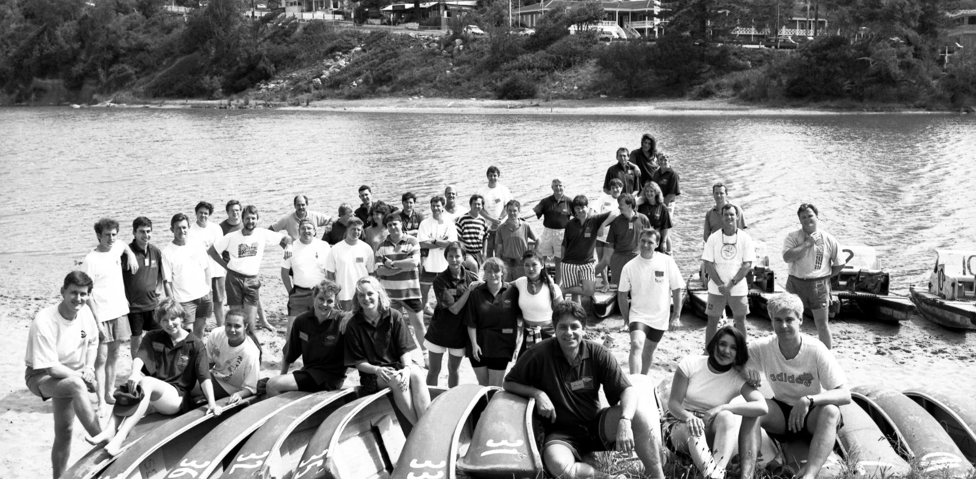 Black and white photograph of colleagues posing for a photograph on a jetty at the beach