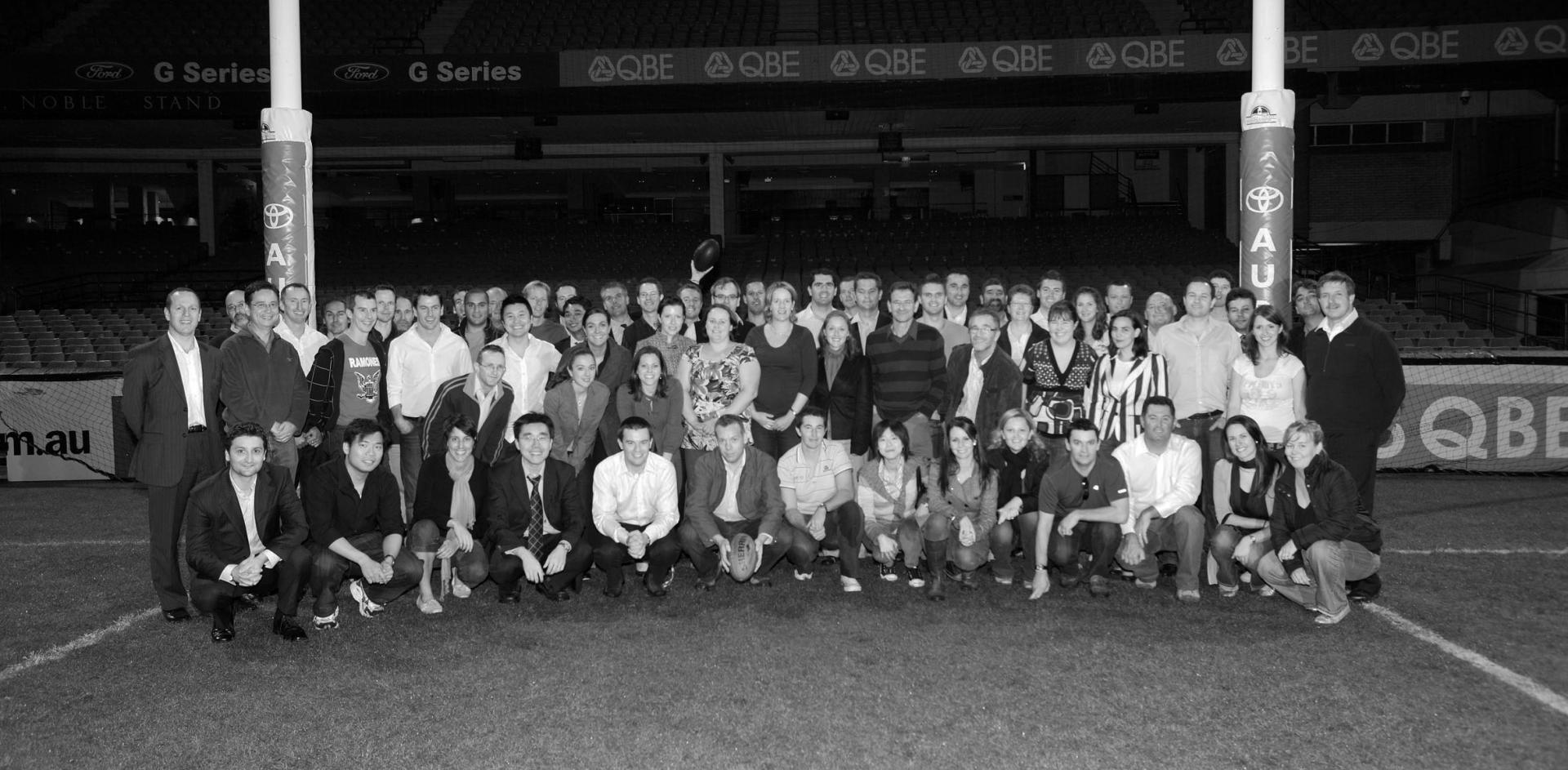 Black and white photograph of APP employees on a rugby field underneath the goal posts