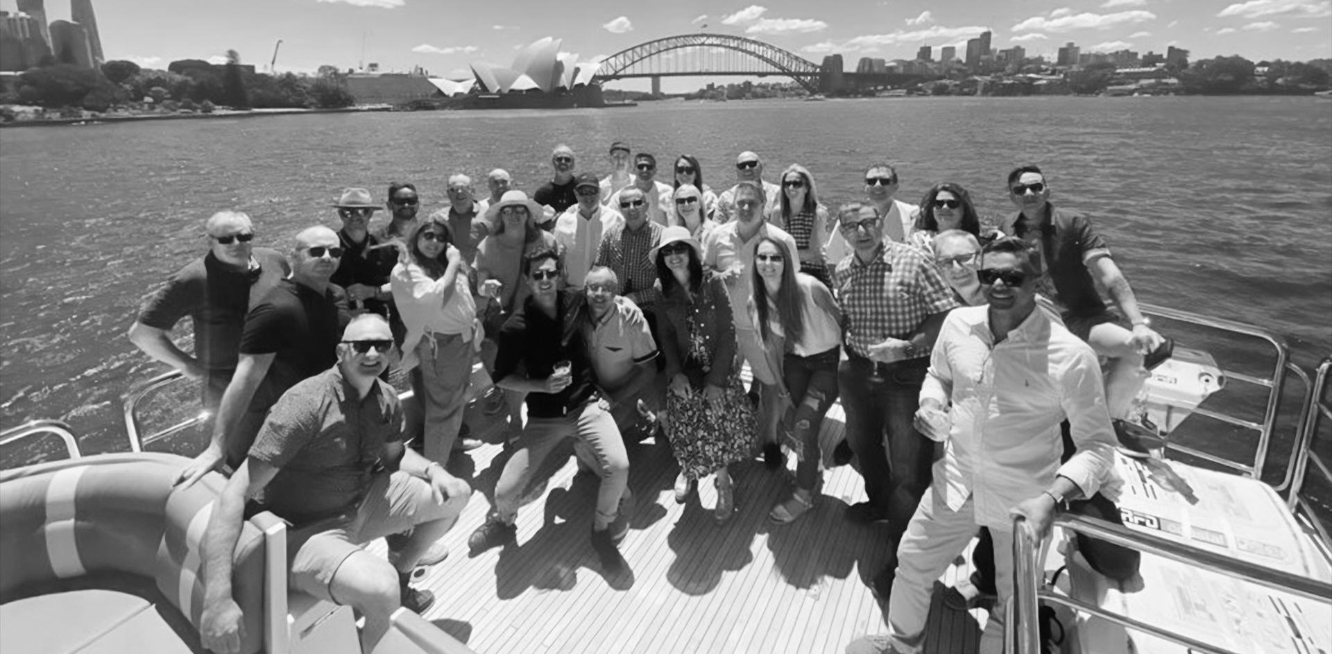 Black and white photograph of a group of people on a boat in the Sydney harbour with the Sydney Harbour Bridge in the background
