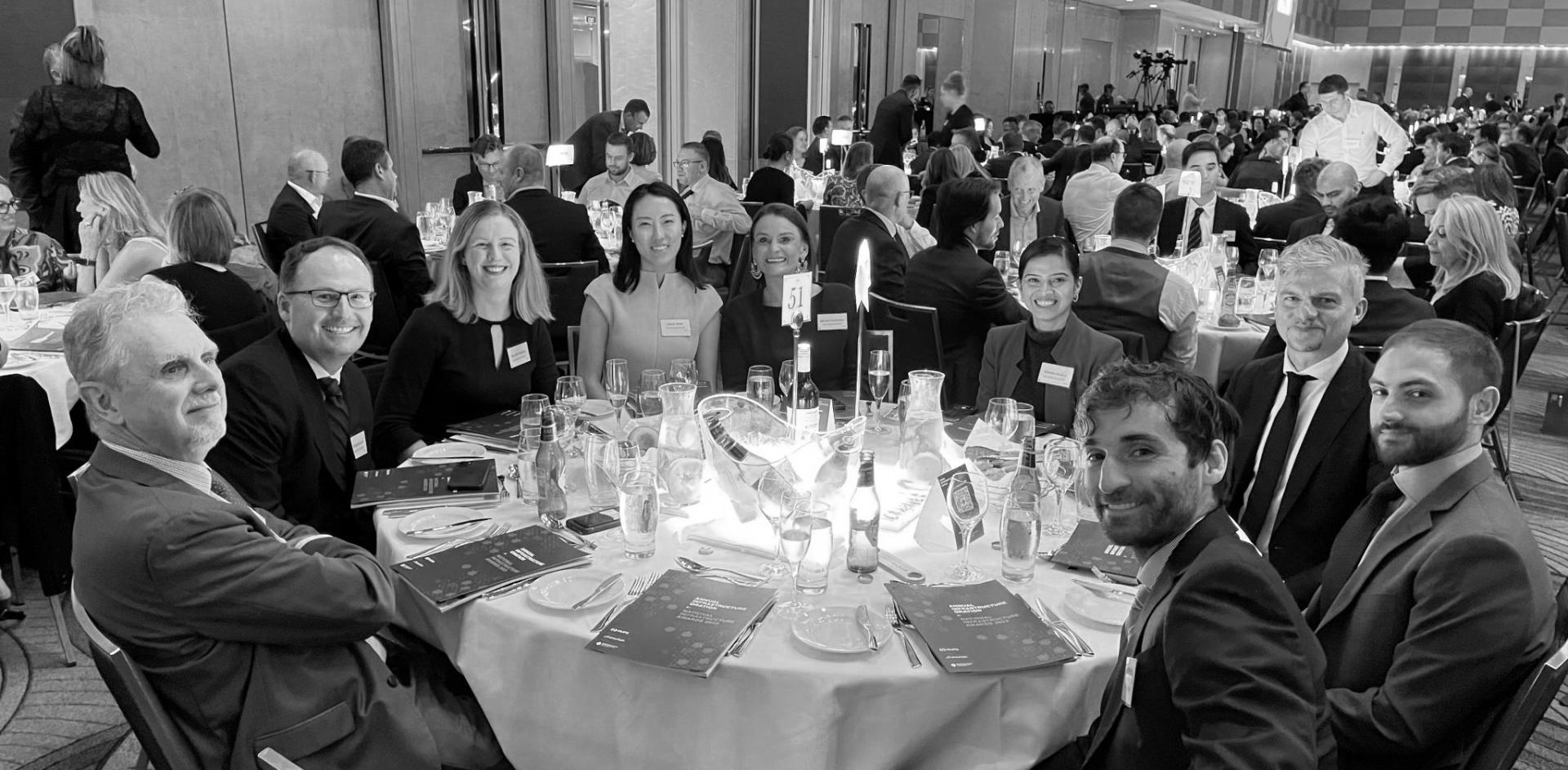 Black and white photograph of a group of people at a conference dinner sitting around a round table smiling