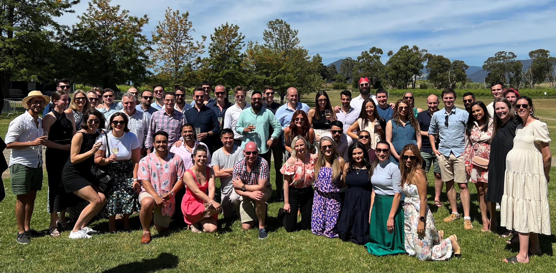 Large group of colleagues pose for photograph in a large park on a sunny day