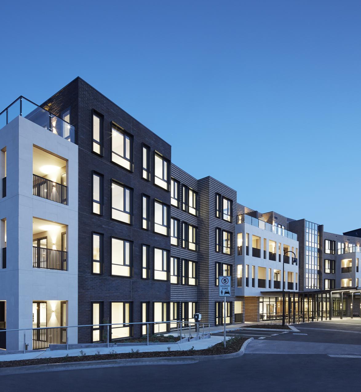 Exterior view of apartment block painted white and back, with lights on